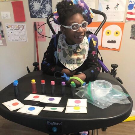 Child with glasses using the functionalhand® to participate in a color activity in a classroom