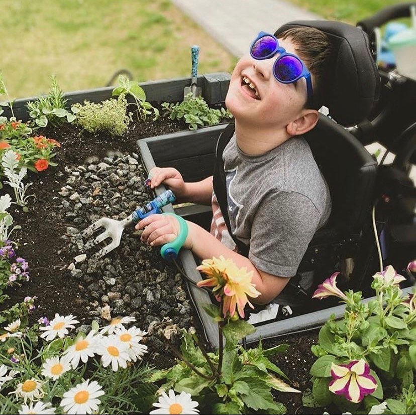 Young boy using the functionalhand® to hold gardening tools to weed a flowerbed.