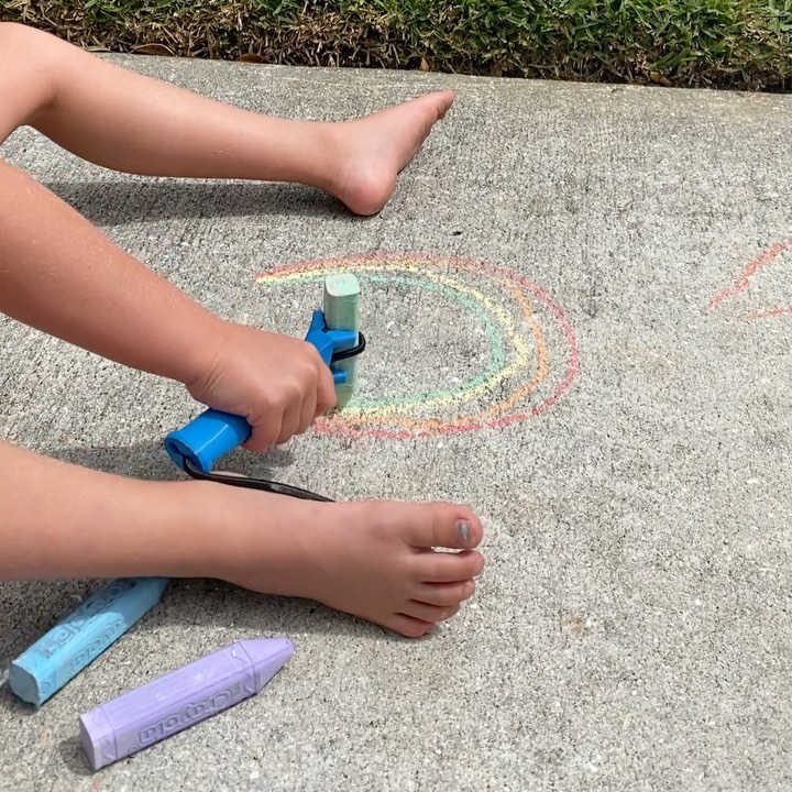 A young girl draws a rainbow with sidewalk chalk using the functionalhand® to help her grip the chalk. 