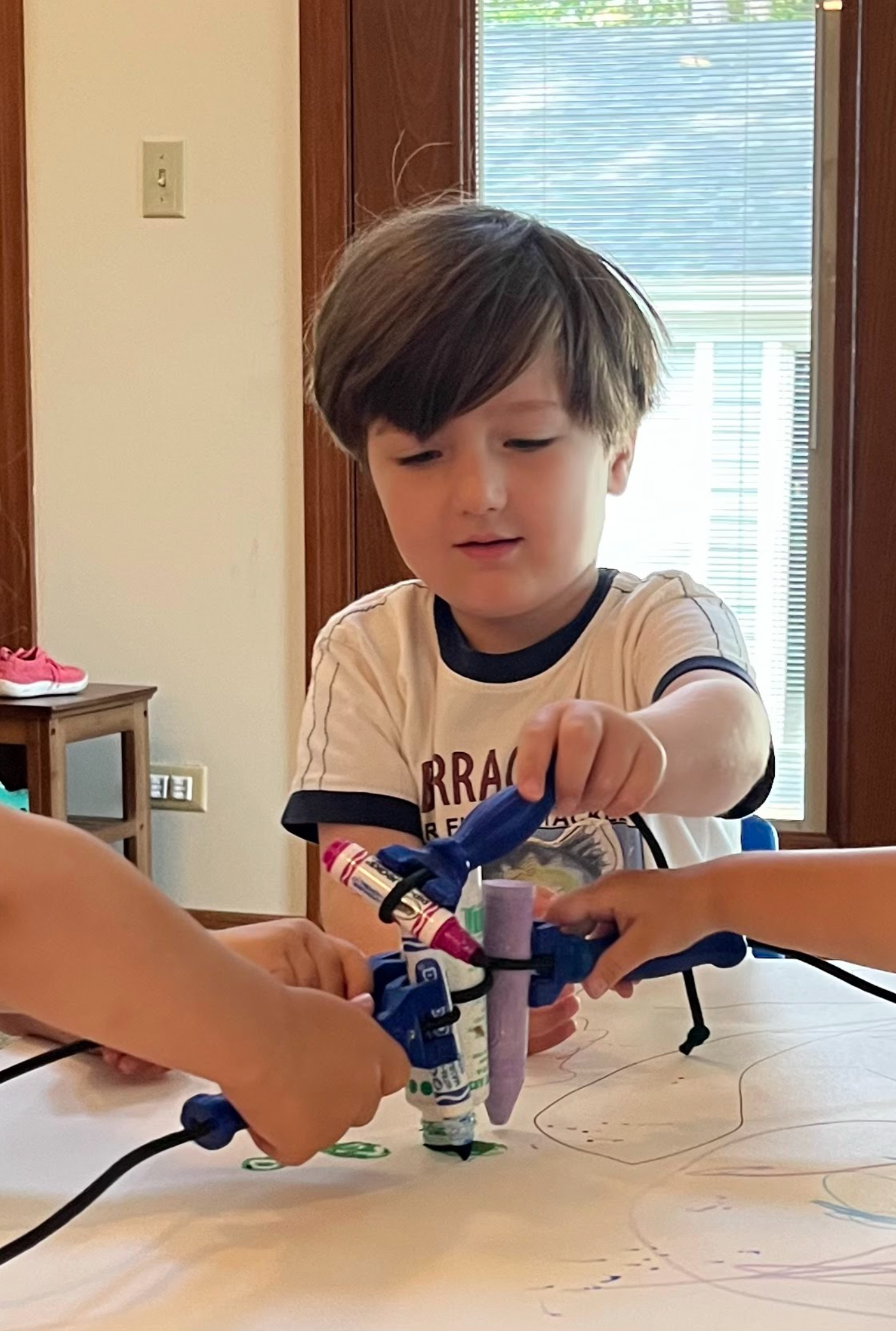 A young child uses the functionalhand® mini to hold a crayon while drawing in a group activity. The assistive device, designed for very young kids with disabilities, helps them grip and participate alongside peers.