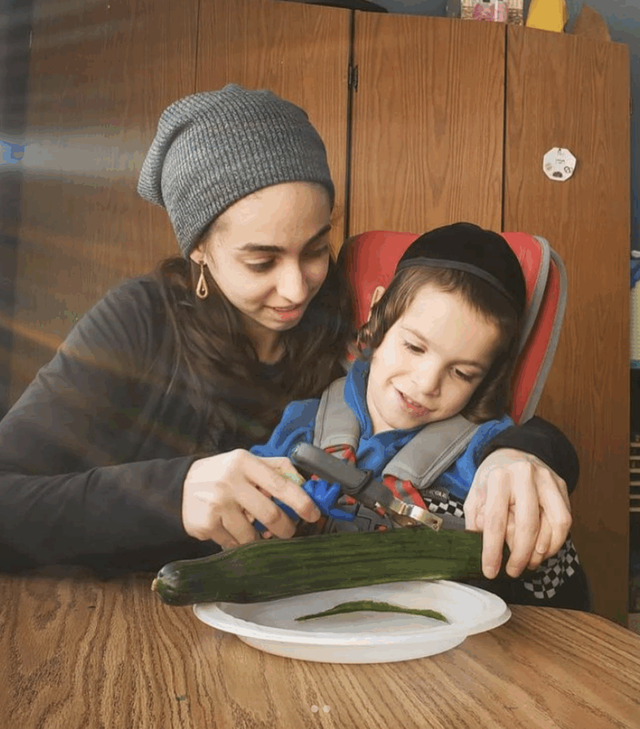 Adult and child using the FunctionalHand assistive device to hold a vegetable peeler and prepare food during daily kitchen routines.