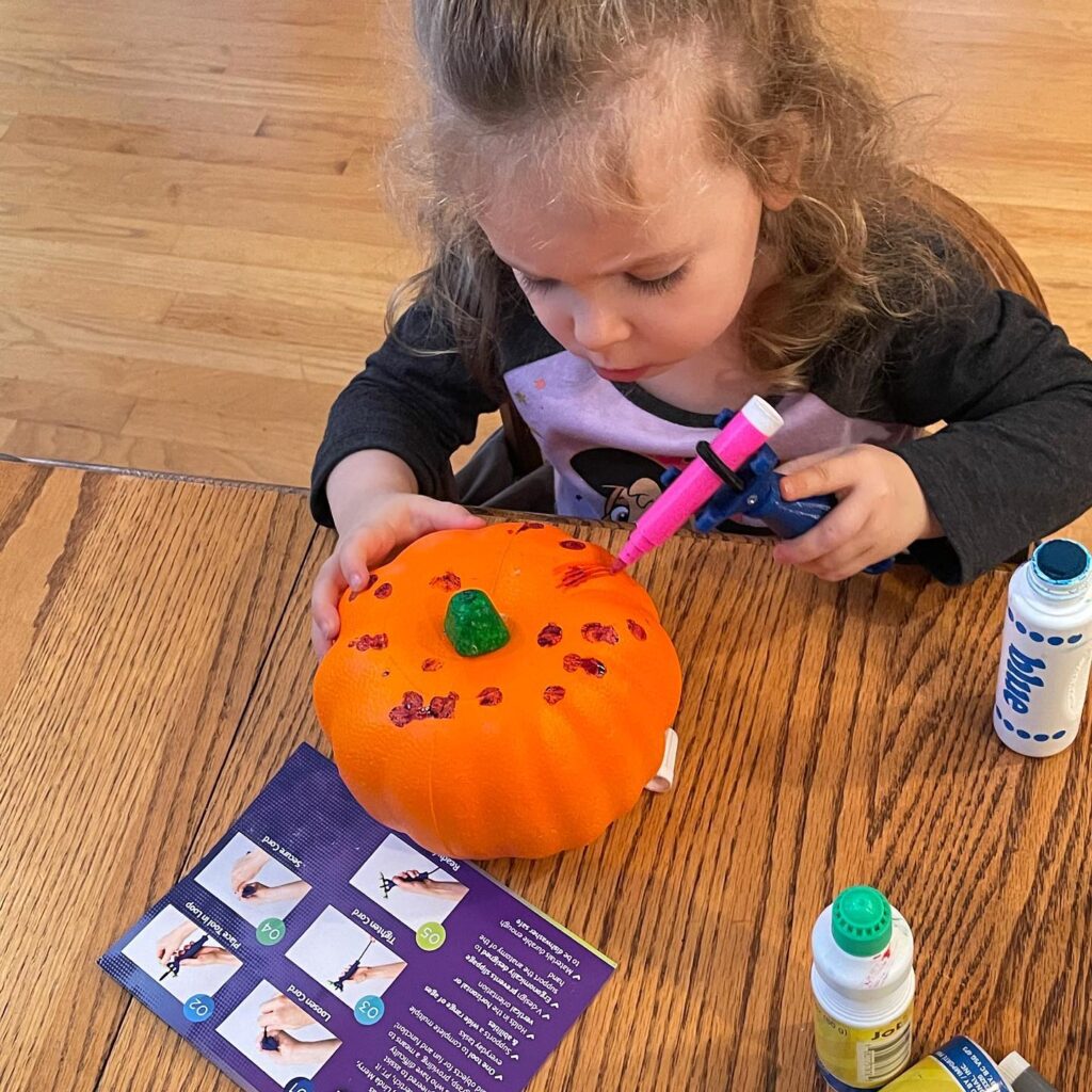 Inclusive Halloween activity for child. Preschool girl sitting at a table and using marker to color a pumpkin using the functionalhand
