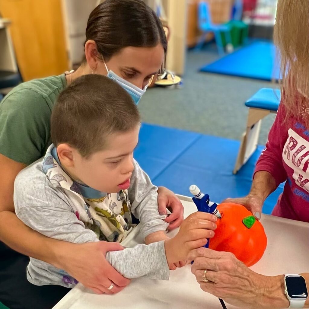 Inclusive Halloween activity for child. Boy with Down's syndrome using the functionalhand and marker to paint on pumpkin.