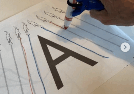 Person using the functionalhand® to trace the letter A while practicing their writing.